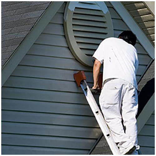 contractor on ladder painting exterior vinyl siding dark green